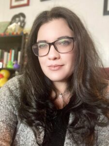 A brown-haired, light-skinned woman with glasses poses in front of a bookcase.